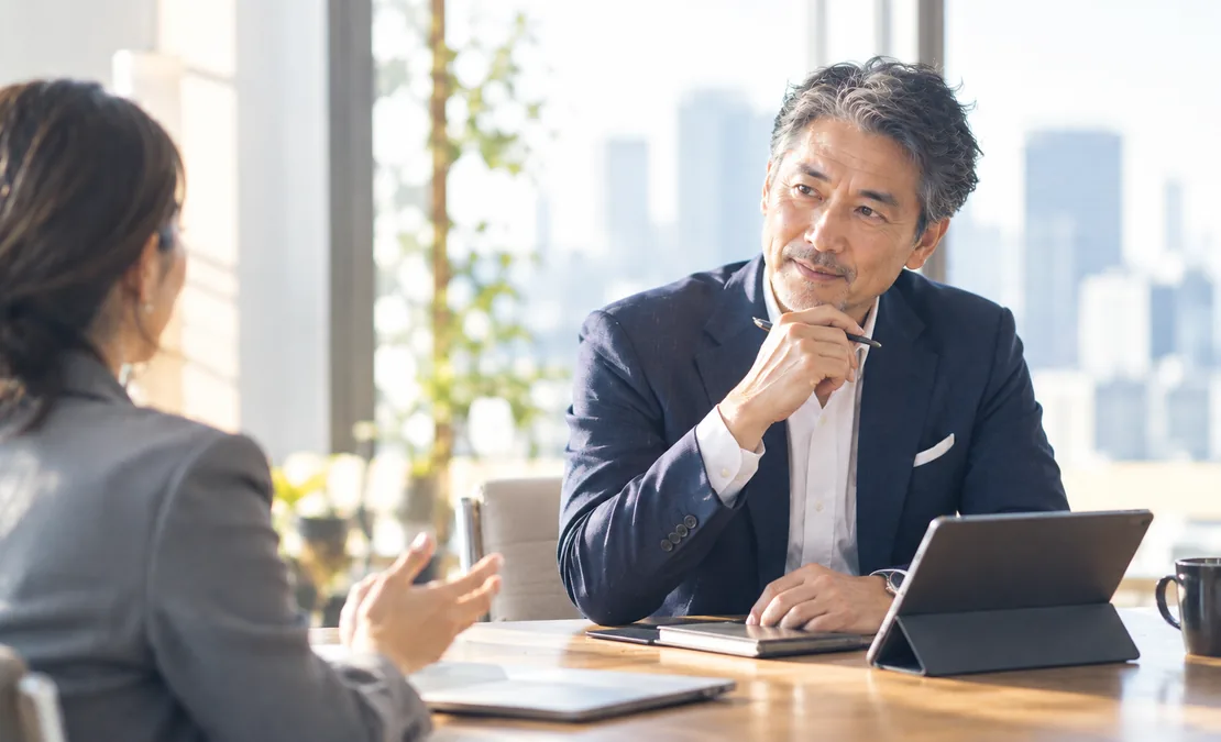 事業責任者が会議室でマネージャーの報告を聞き、判断を下そうとしている様子