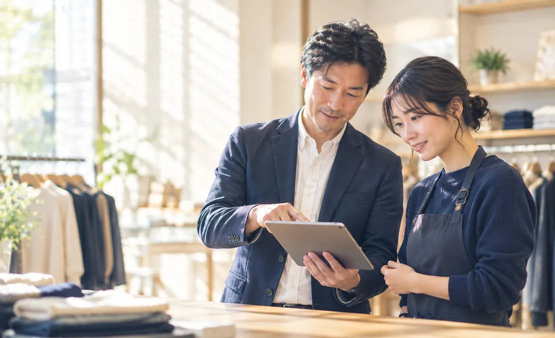 店長と店舗スタッフがアパレル店舗のカウンターでタブレットを一緒に見ながら打ち合わせている様子